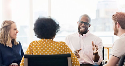 Četiri osobe sede zajedno i razgovaraju. Jedna osoba gestikulira rukama 