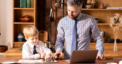 Muškarac u košulji i sa kravatom radi na laptop računaru, a dete u sličnoj odeći radi nešto na tabletu 