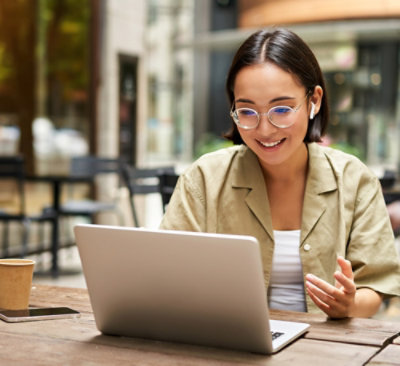 A woman wearing glasses and a tan jacket using a laptop.