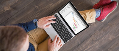 Una persona indossa una maglia blu e scarpe rosse, è seduta sul pavimento di legno e digita sul portatile.