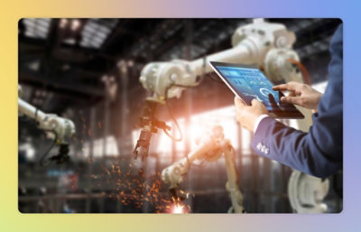 A person in a factory controls robotic arms using a tablet, highlighting advanced automation technology.