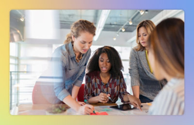 Four women collaborating over documents on a table in a brightly lit office.