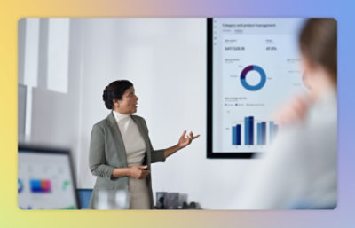 A person in professional attire is giving a presentation with charts and graphs displayed on a screen