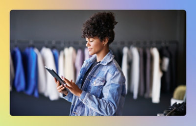 A woman in a denim jacket is using a tablet in a clothing store
