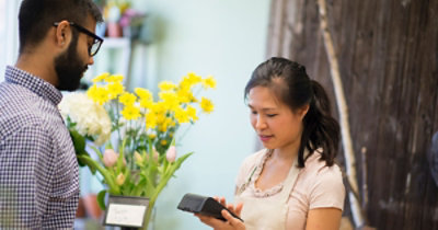 Menadžer prodavnice obrađuje plaćanje kupcu u prodavnici, a u pozadini se nalazi buket cveća.