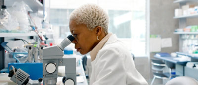 A woman in a lab coat looking through a microscope