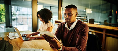 שני אנשים עובדים במשרד. אדם אחד משתמש במחשב נישא והאחר מחזיק טאבלט.