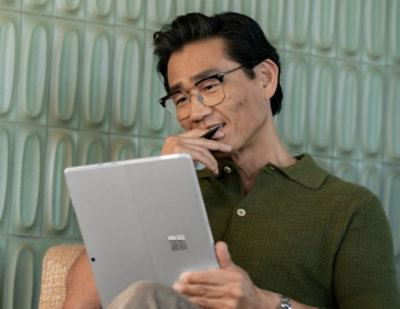 Smiling woman at desk using tablet and monitor for work.