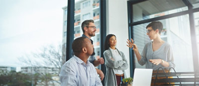 Four colleagues are having a discussion in a modern office with large windows.