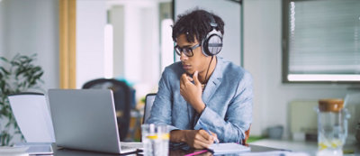 Una persona indossa cuffie seduta alla scrivania e guarda lo schermo di un computer con una mano sul mento