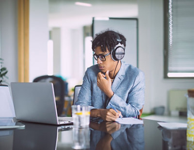 A person wearing headphones sits at a desk working on a laptop