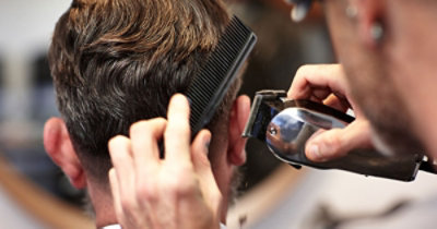 Berberin sa češljem u ruci podrezuje kosu muškarca električnim makazama.