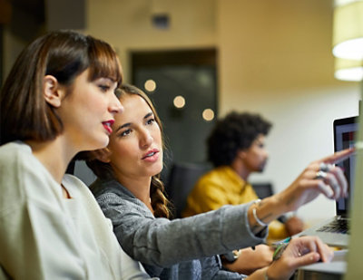 Two women are sitting and discussing something on a computer screen