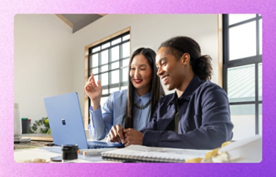 Two coworkers reviewing notes beside a laptop at a desk.