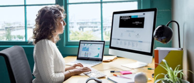 Person working at desk with laptop and desktop monitor.