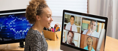A woman with curly hair is on a video call with five people, visible on her computer screen.