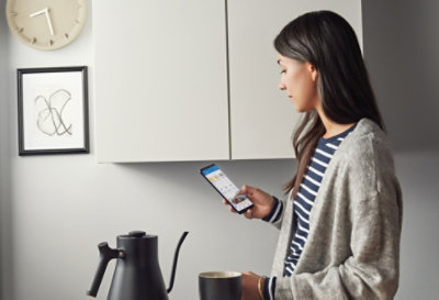 Een persoon die in een keuken staat en OneDrive op een mobiel apparaat gebruikt.