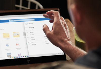 Een persoon die een laptop gebruikt en de versiegeschiedenis van een document bekijkt in OneDrive.