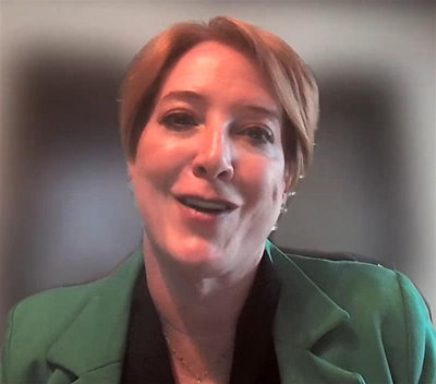 Person wearing a green blazer sitting indoors against a neutral background.