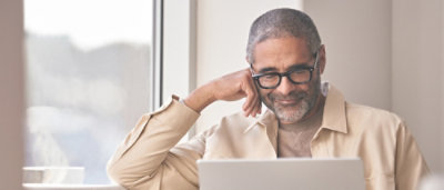A man wearing specs smiling and working on the laptop