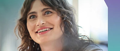 A close-up of a woman's face with curly dark hair, smiling.