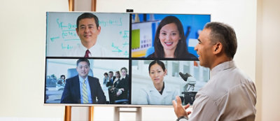 A group of people participate in a video conference call in a modern meeting room.