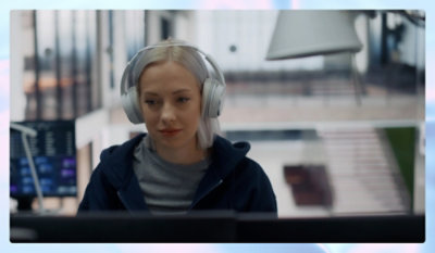 אדם עם אוזניות גדולות וקפוצ'ון כהה, יושב ליד שולחן עם מסכי מחשב במשרד מודרני.