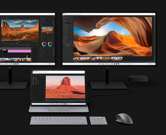 Surface Laptop Studio gedockt aan twee grotere monitoren die worden gebruikt om video te bewerken.