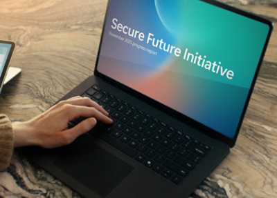 Laptop screen shows “Secure Future Initiative, November 2025 progress report.