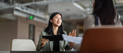 A woman holding a tablet and talking to another woman.