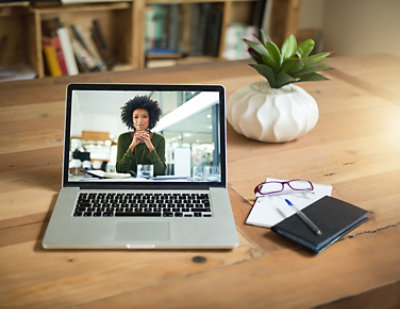 A woman on a laptop screen with her hands folded in front of her face.