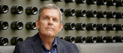 A man sitting with white hairs and weared a shirt.