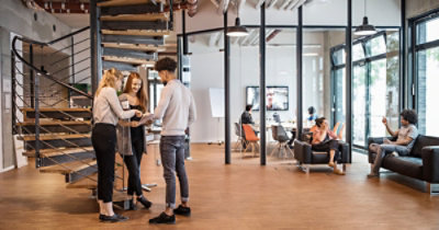 Persone in piedi parlano accanto alle scale in un ufficio moderno con ampie finestre.