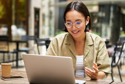 Person working on a laptop at an outdoor cafe table with a disposable coffee cup beside them.