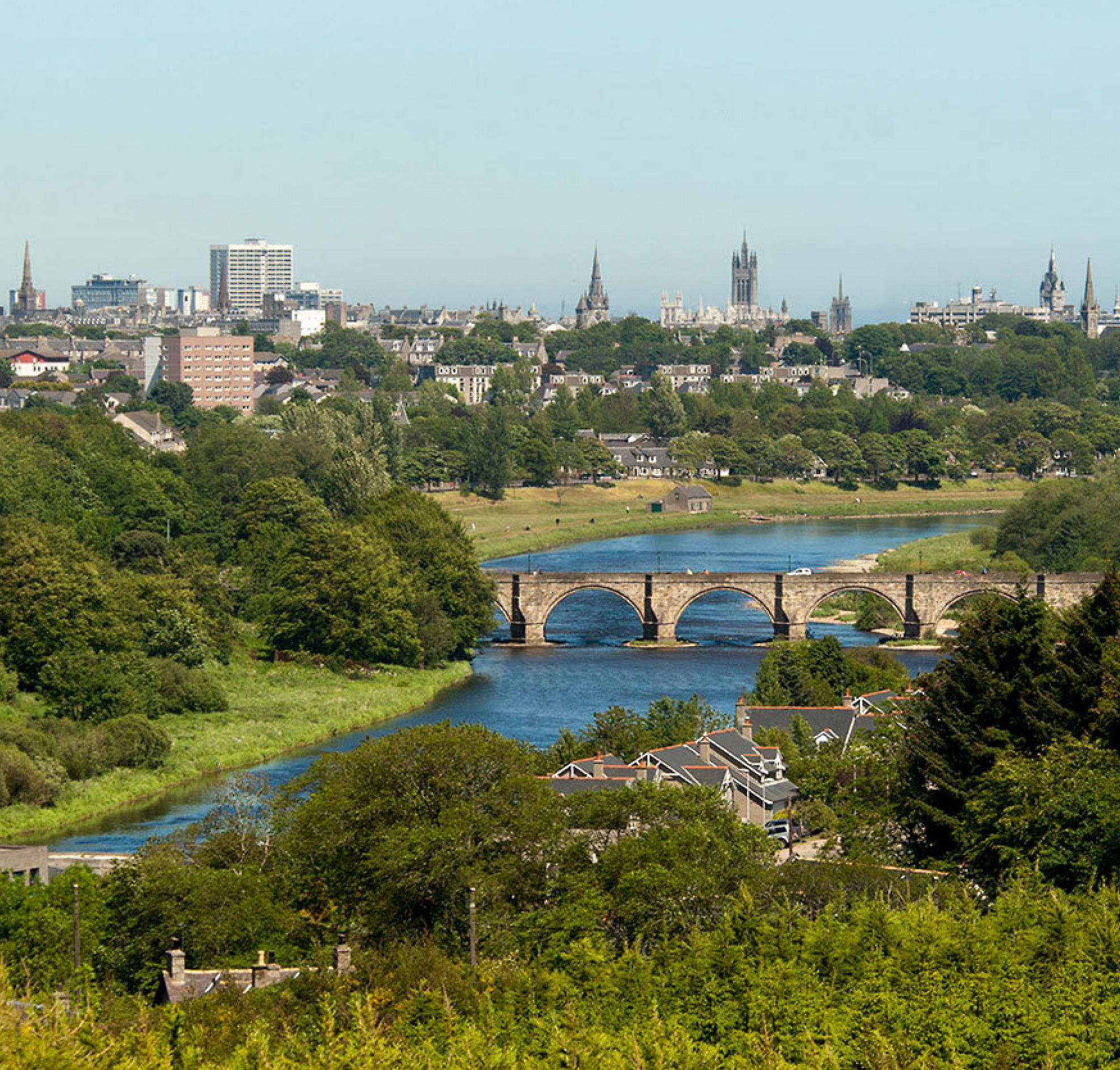 Hình ảnh từ trên không nhìn xuống thành phố với cây cầu đá bắt chéo dòng sông, được bao quanh bởi cây xanh và sự kết hợp với khung cảnh hiện đại 