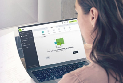 A person views a tax preparation software interface on a laptop screen while holding a document.