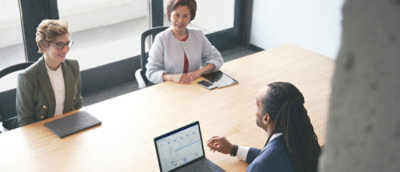 Three professionals discuss over a laptop in a bright, modern office setting.