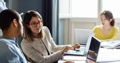 Colleagues collaborating at a table using laptops in a bright office