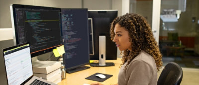 Person coding at a workstation with multiple monitors in an office