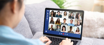 Person participates in a video conference on a laptop, with multiple attendees visible on the screen.