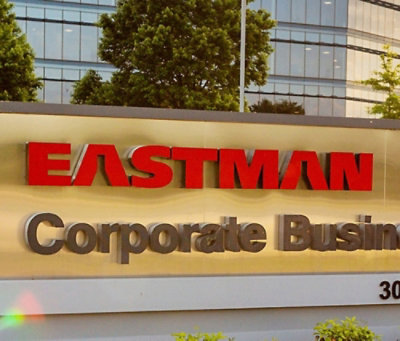 A red sign with white text and the partial word EASTMAN visible, with a building and trees in the background.
