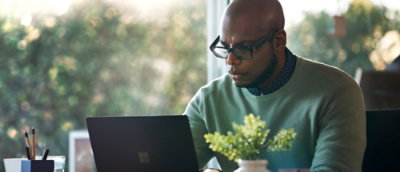 A man wearing glasses and a green shirt looking at a laptop.