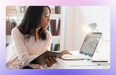 A woman working on laptop and also holding a tablet.
