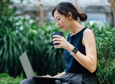 Person using a laptop outdoors with a coffee.