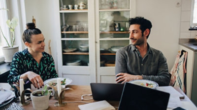 A person and another person sitting at a table with a computer