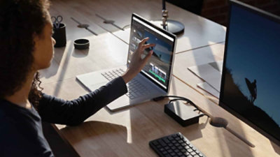 Osoba sedi za stolom na kojem se nalazi eksterni čvrsti disk i koristi funkcije ekrana za unos dodirom na laptop računaru koji prikazuje softver za uređivanje video zapisa