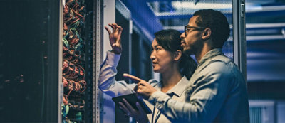 Due persone esaminano un rack di server in un data center, precisano dettagli e discutono mentre uno ha in mano un tablet.