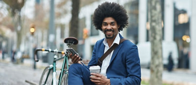 A person sitting on a bench holding a cup and a phone