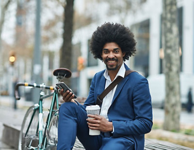 A man sitting on a bicycle holding a phone and a cup of coffee.
