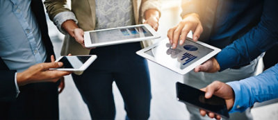 Quattro persone discutono e interagiscono tramite smartphone e tablet.